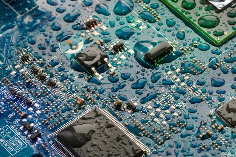 The circuit board of the motherboard is covered with drops of water in blue-green tones.